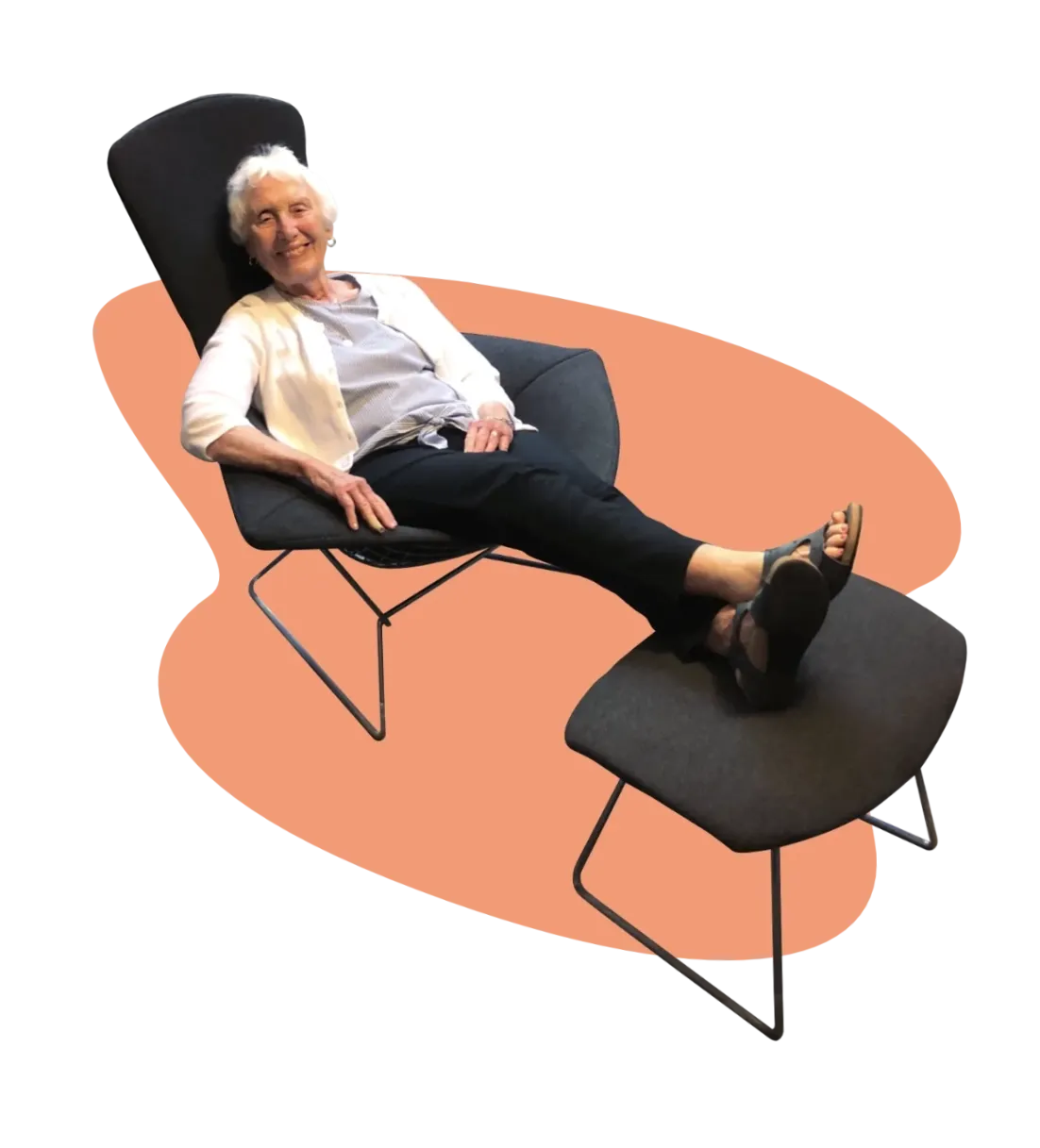 Happy woman seated in charcoal gray Harry Bertoia Bird Lounge chair with feet propped on matching ottoman